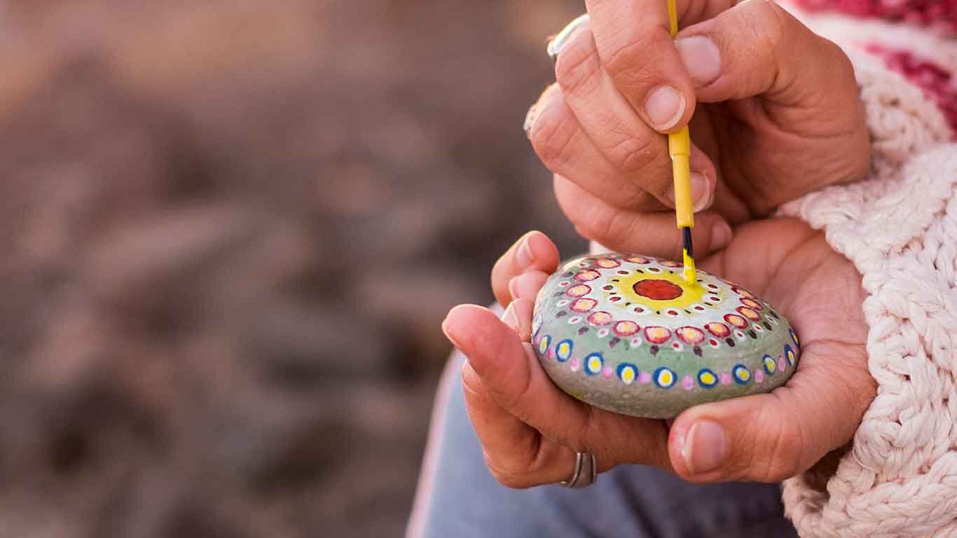 Een vrouw beschildert een steen met een mandala. 